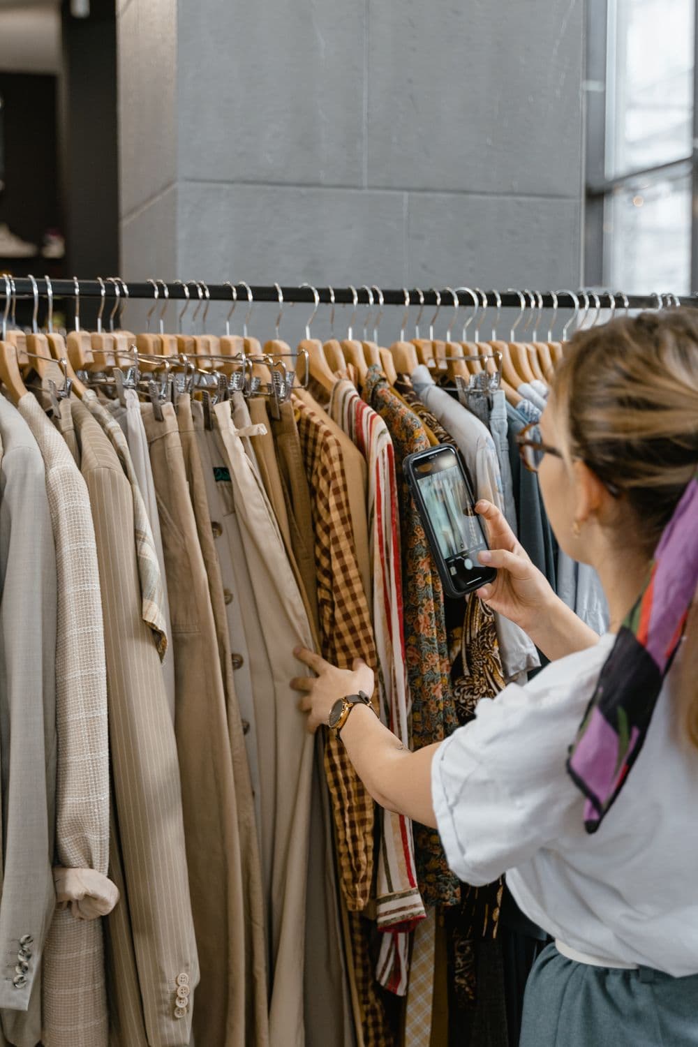 Seller taking photos of outfits on a clothing rack with a smartphone